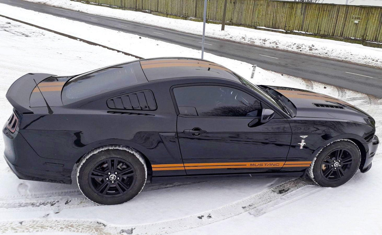 Black Mustang with racing stripes parked on snow-covered road, showcasing sporty vinyl decals.