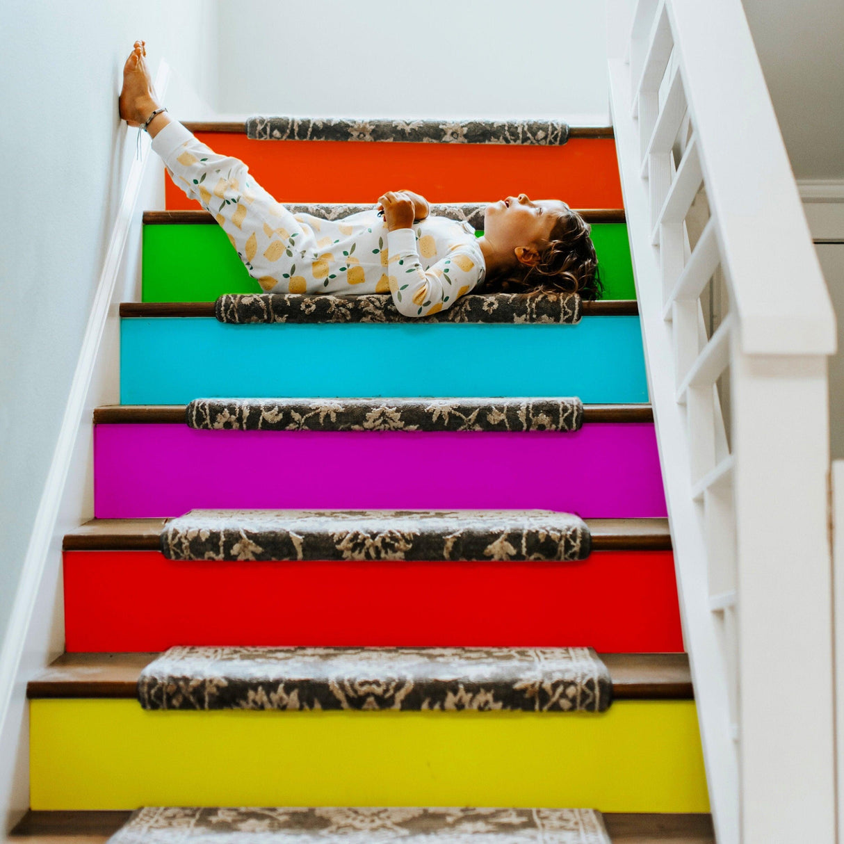 Child relaxing on colorful stairs decorated with vibrant stair riser decals by VibrantStep™.