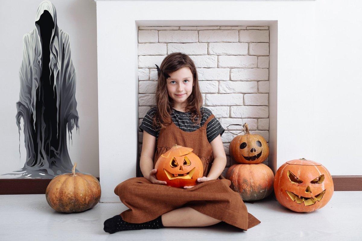 Girl with pumpkin sitting in front of a wall sticker of a ghostly figure, surrounded by carved pumpkins.
