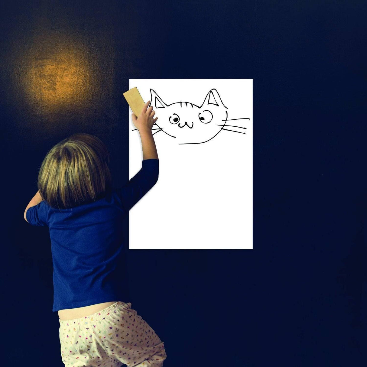 Child drawing on a versatile dry erase vinyl decal with a cat sketch on a dark wall.