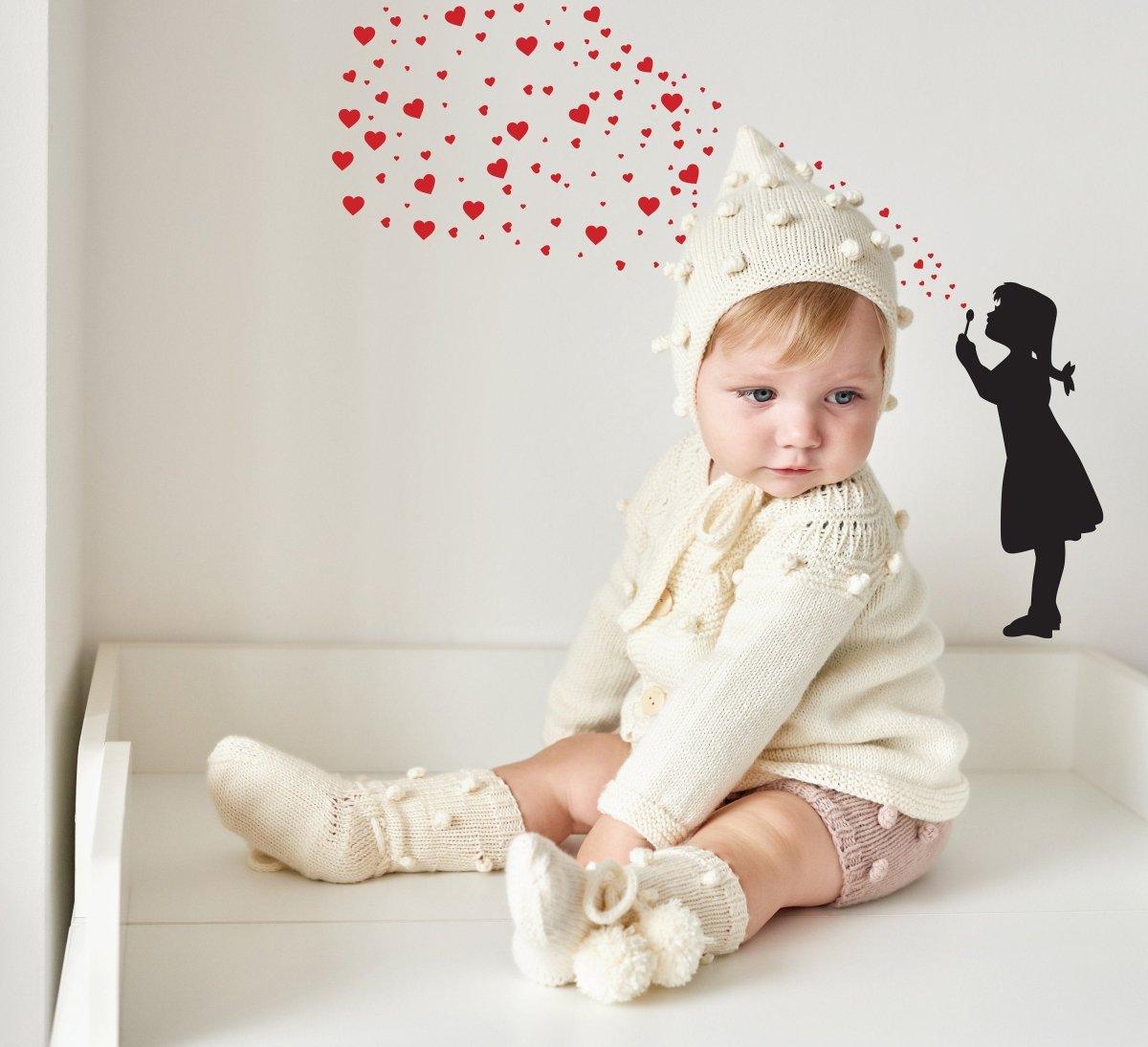 Adorable baby in a cozy cream outfit sitting with heart-shaped bubbles above, alongside a playful silhouette of a girl.