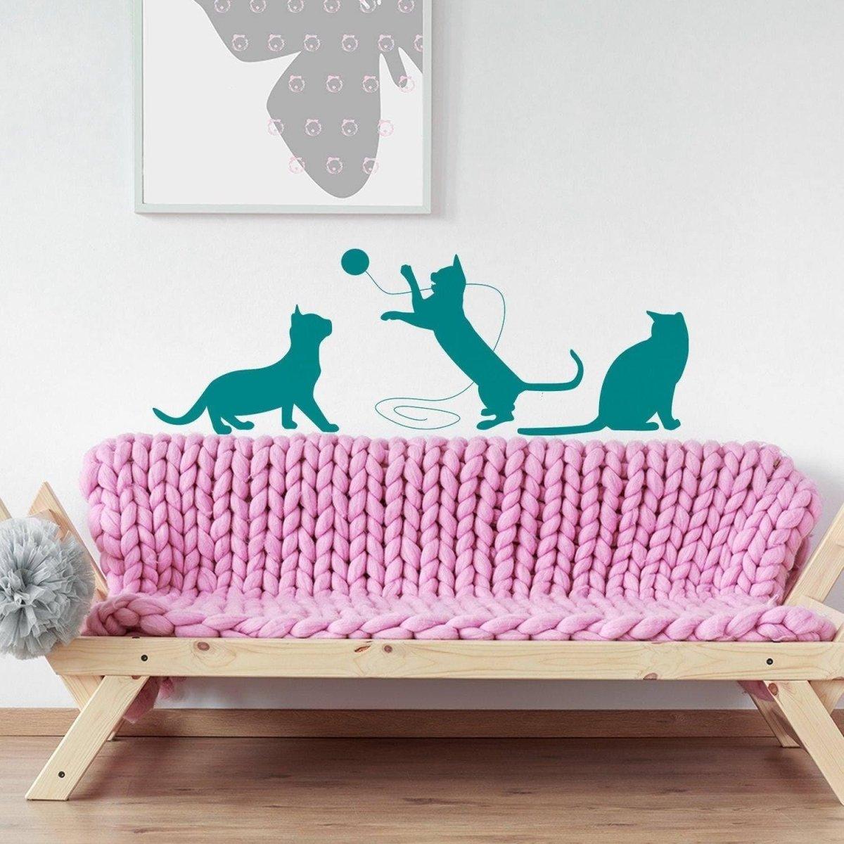 Adorable cat silhouette vinyl decal featuring playful cats on a pink knitted sofa, perfect for pet-themed wall decor.