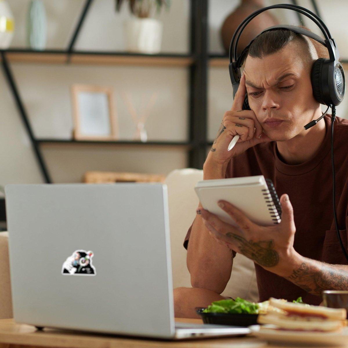 Man with headphones contemplating while using laptop decorated with contemplative monkey vinyl sticker.