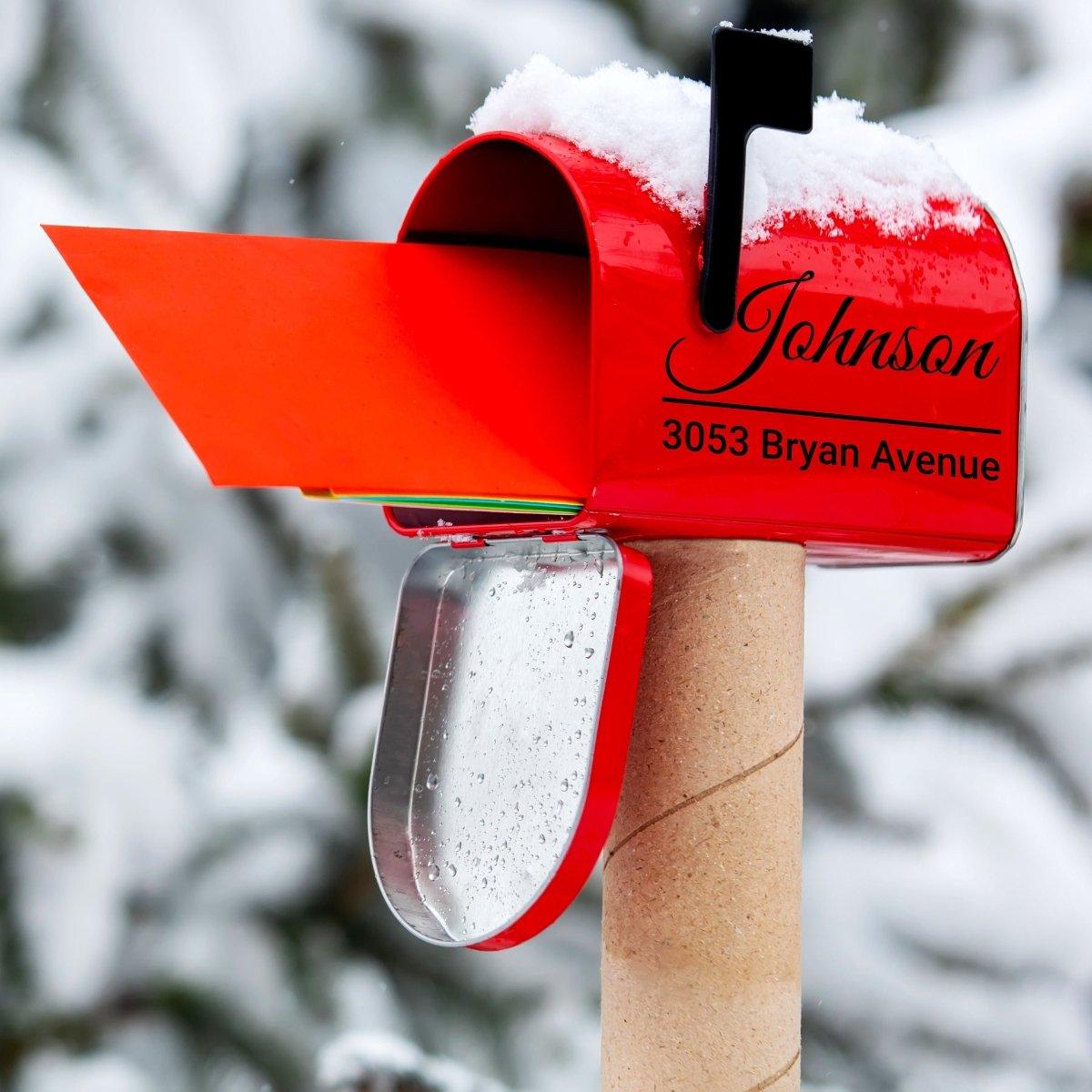 Personalized red mailbox with cursive name decal and house number, surrounded by snow.