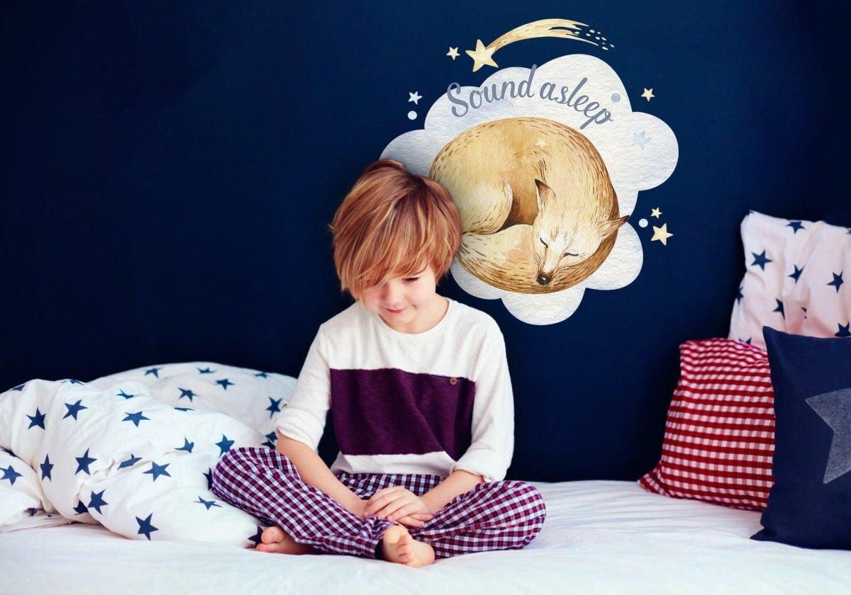 Child sitting on bed with starry sheets, beside dreamy fox wall sticker in cozy nursery decor.