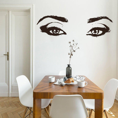 Elegant vinyl wall decal of a woman's eyes above a wooden dining table, enhancing room decor with style.