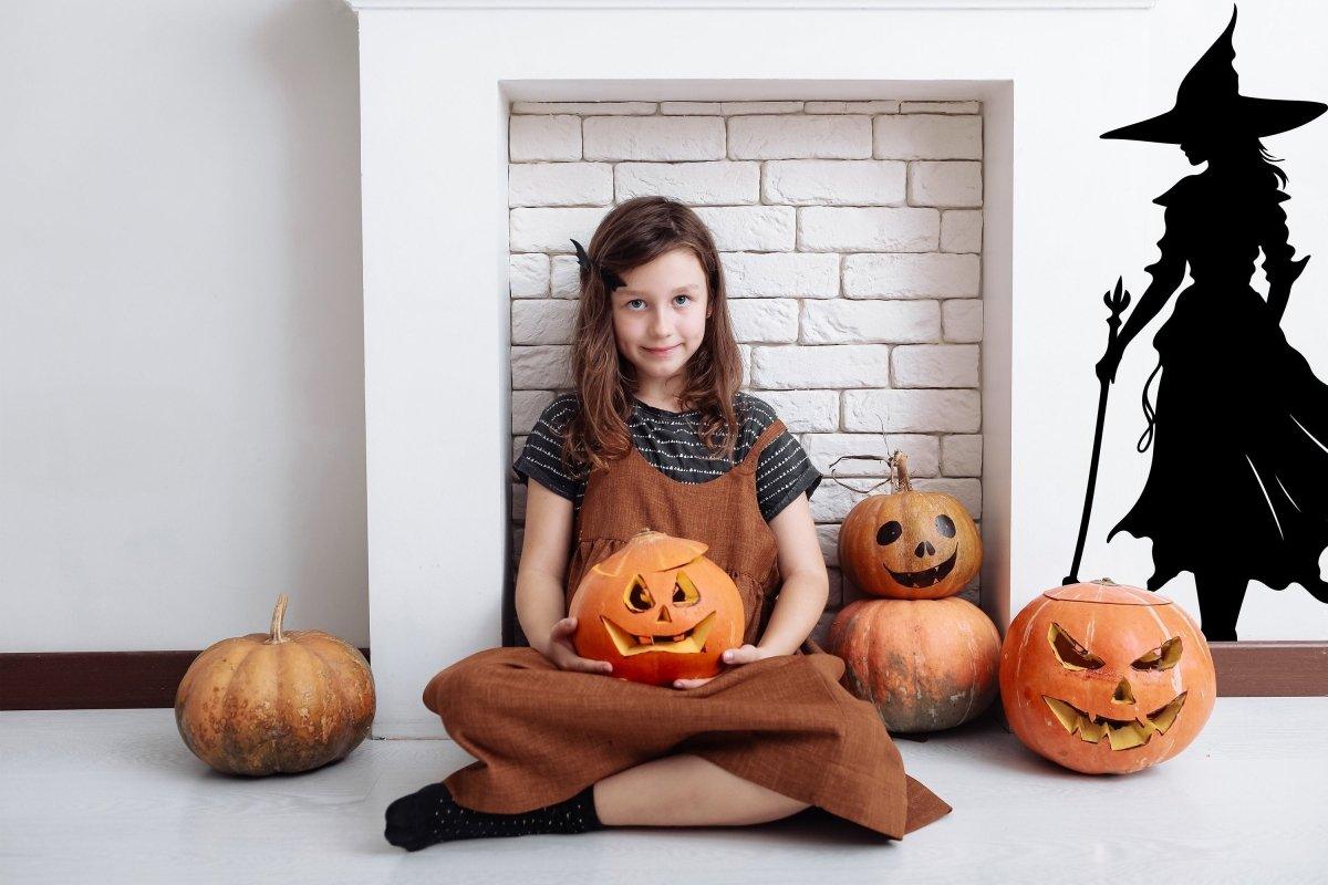 Girl holding a pumpkin with Halloween decorations, including carved pumpkins and a witch silhouette decal.