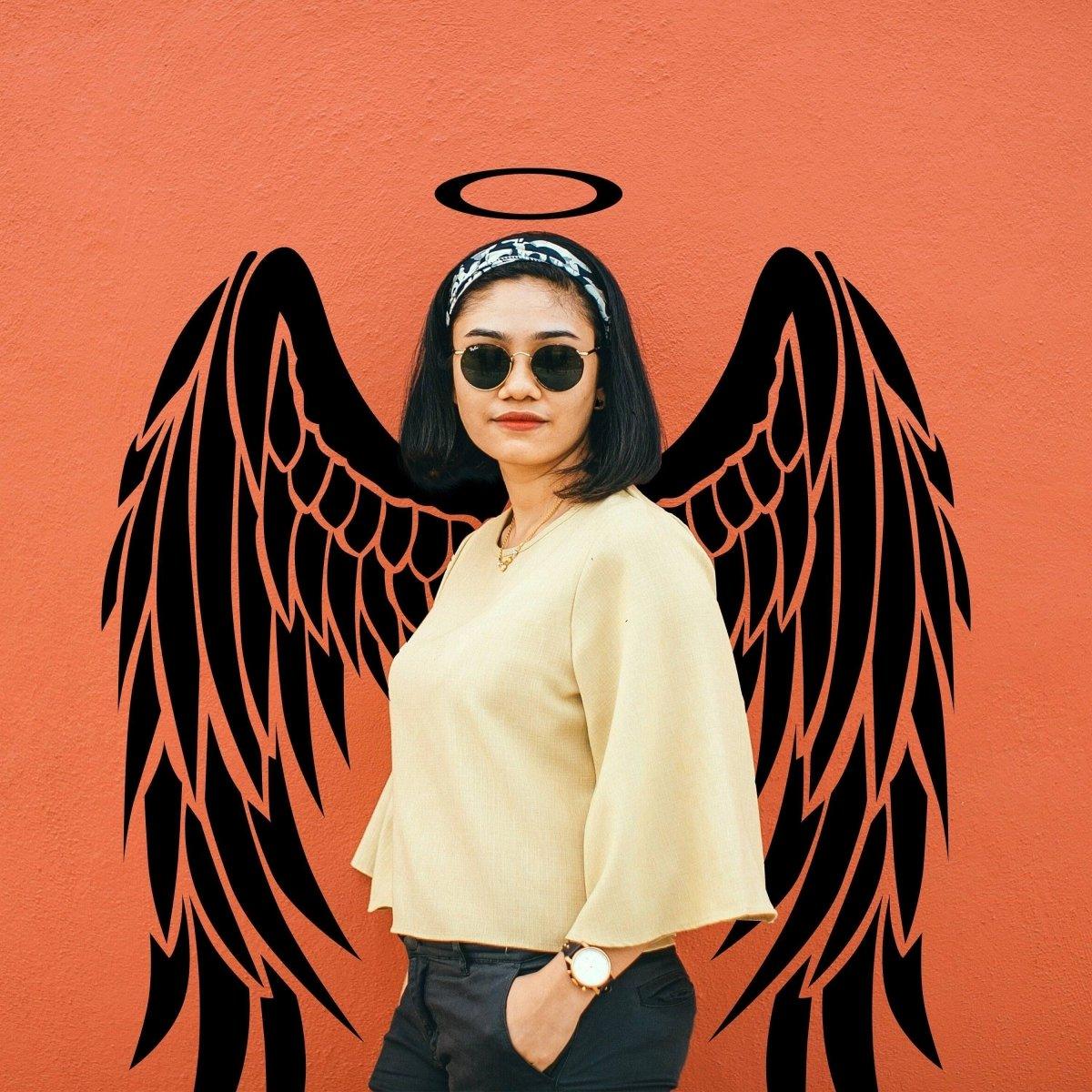 Woman posing with angel wings wall sticker, stylish outfit, sunglasses, against vibrant orange background.