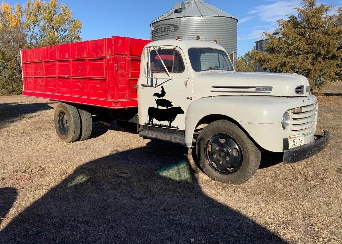 Vintage farm truck with red bed and farm animal silhouette decal on a rural landscape.