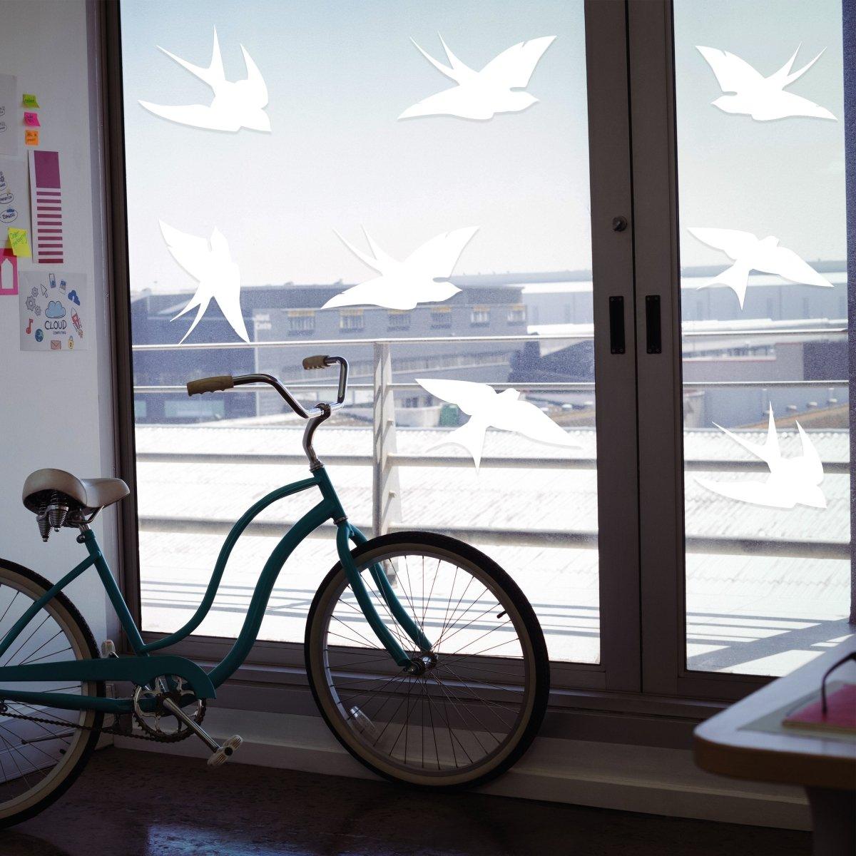Bird safety window decals by FeatherGuard displayed on glass door with bicycle, promoting collision awareness.