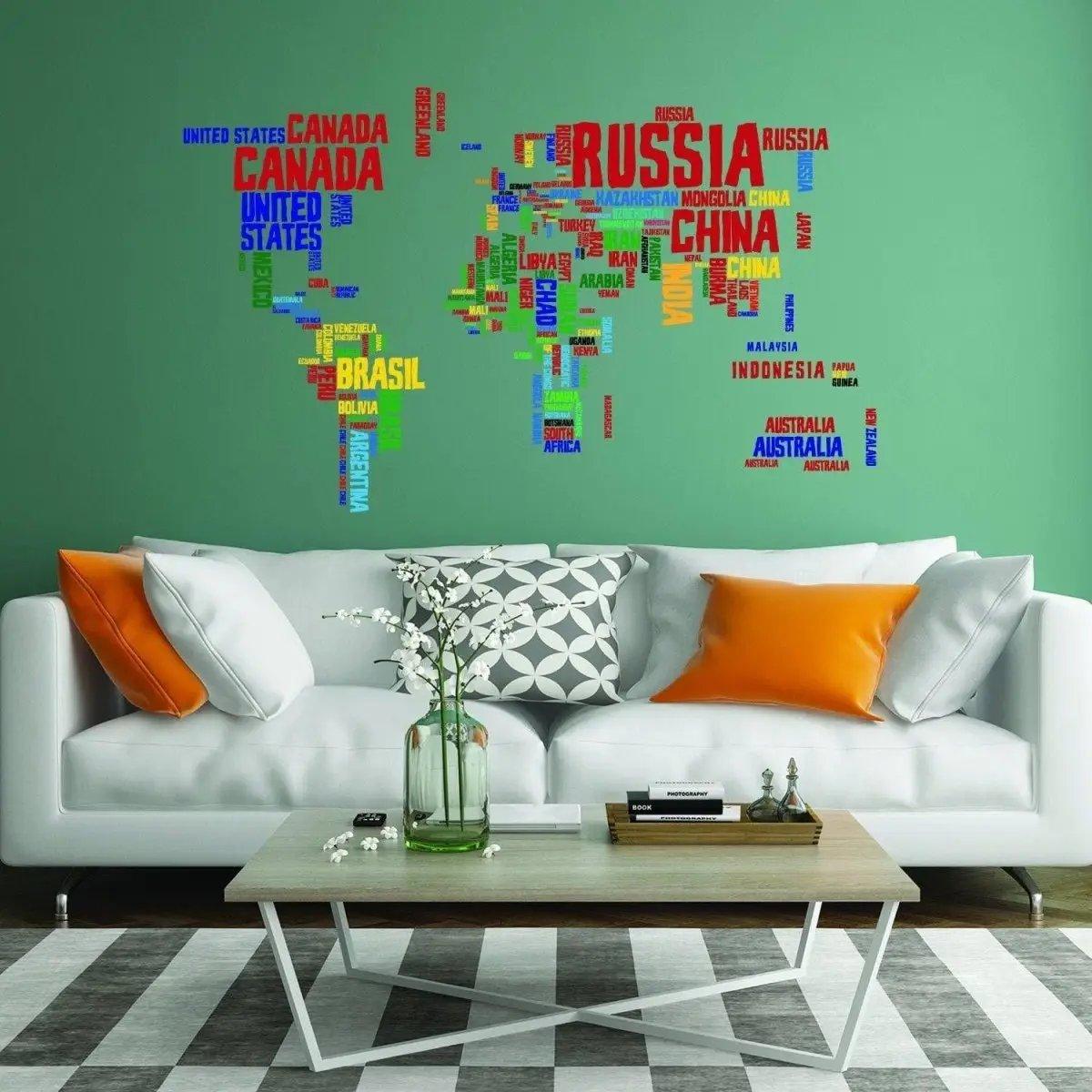 Colorful world map vinyl wall decal with country names on green wall above modern living room sofa and coffee table.