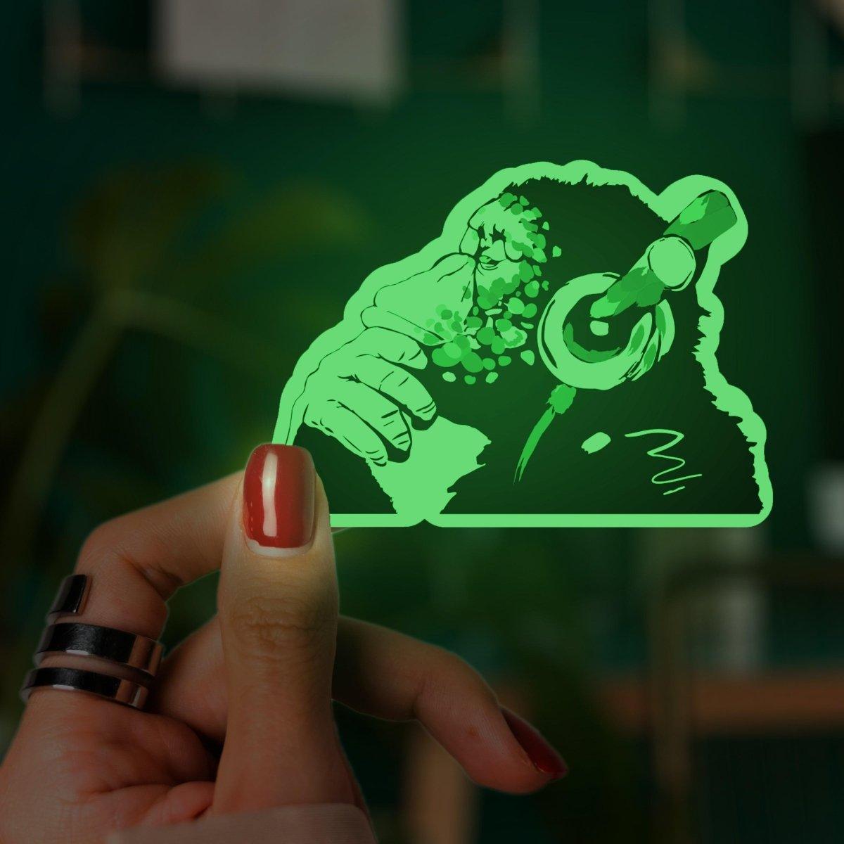 Glow in the dark monkey laptop decal held by hand, featuring a playful design of a monkey with headphones.
