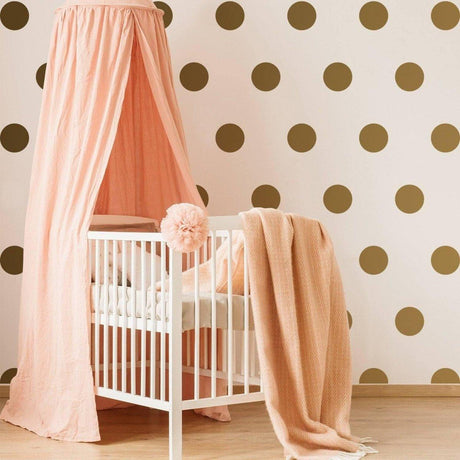 Cozy nursery featuring gold circle wall decals and pink canopy over a crib, adding a magical touch.