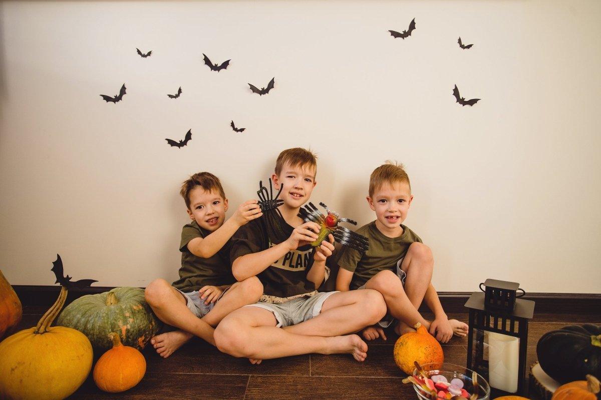 Three boys playing together with Halloween decorations and bat decals on the wall, surrounded by pumpkins.