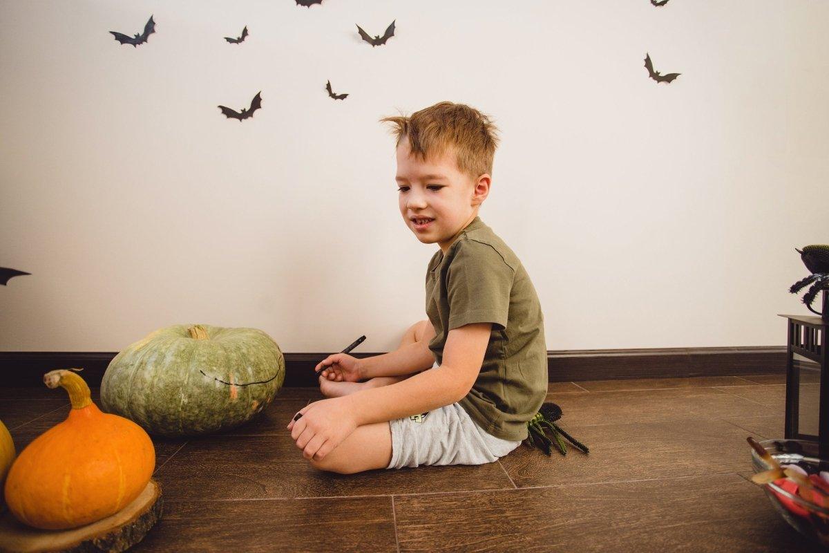 Child sitting on the floor surrounded by pumpkins and spooky bat decals for Halloween decorations.