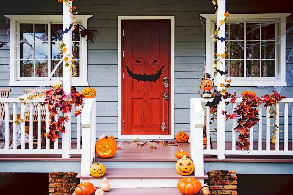 Spooky Halloween porch with monster face door decal, decorated with pumpkins and autumn leaves.