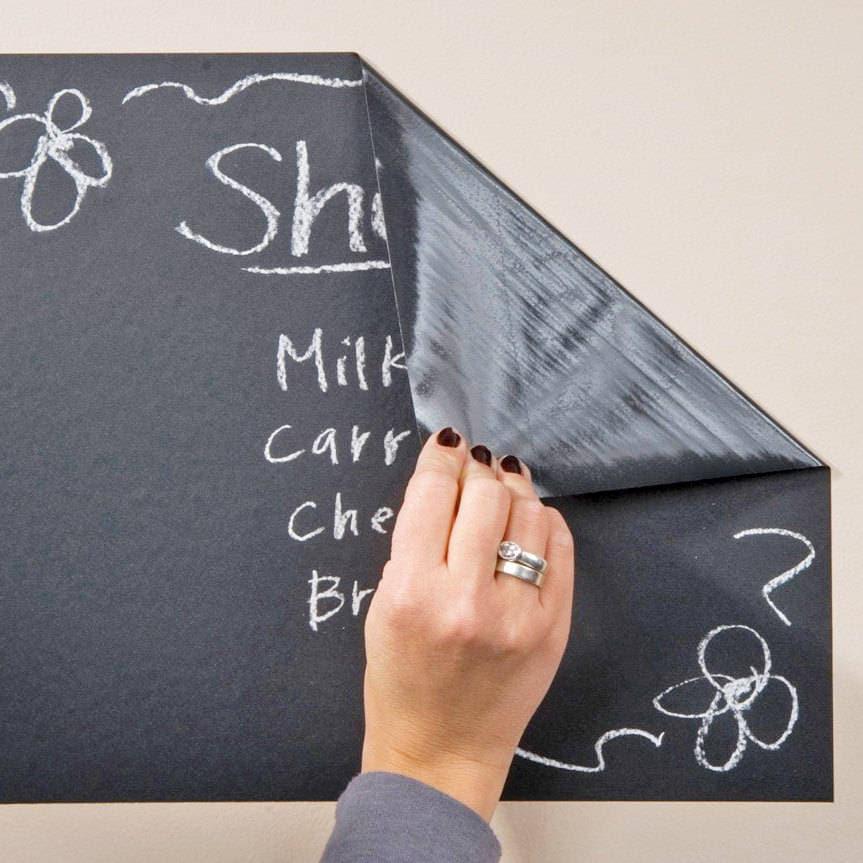 Hand peeling back a chalkboard wall sticker with handwritten notes and doodles on a wall.