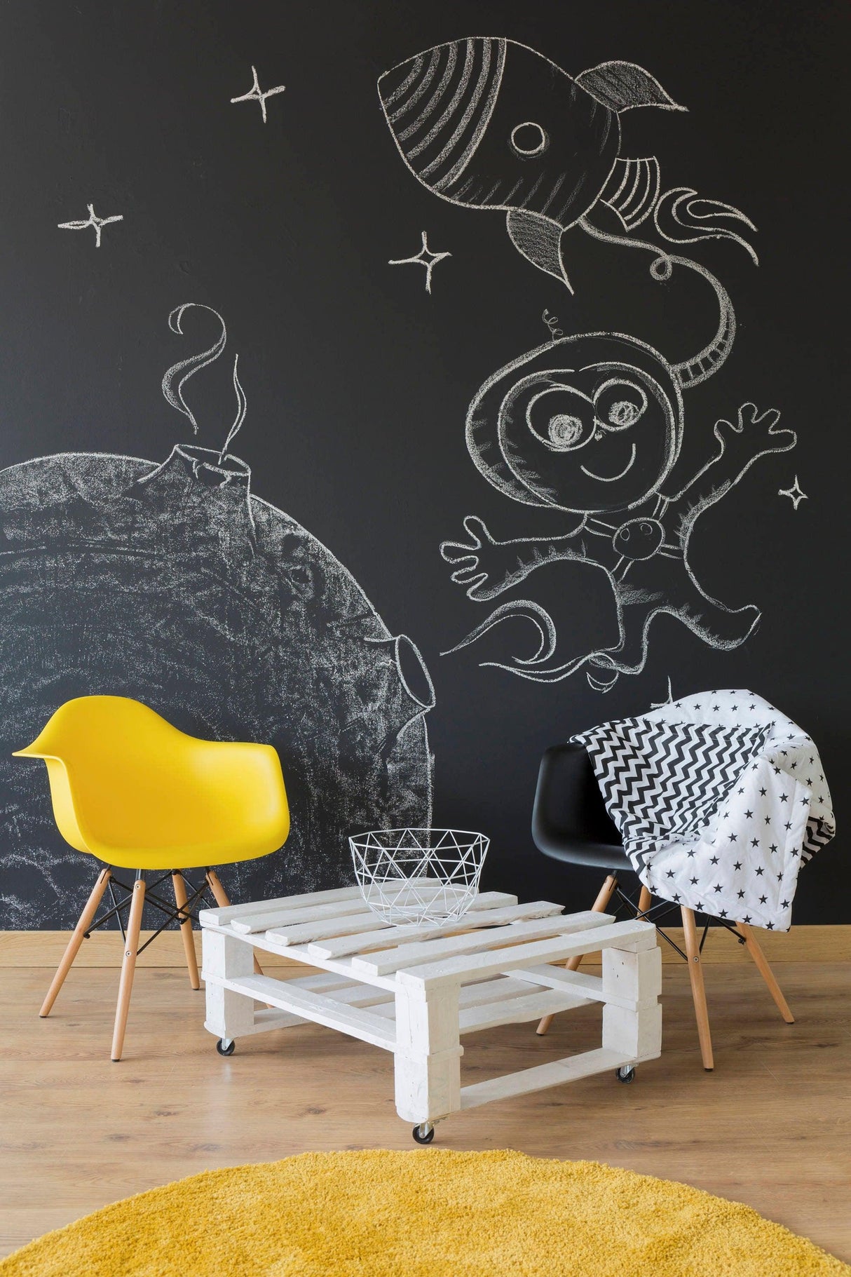 Chalkboard wall with rocket and astronaut drawings, featuring modern furniture like yellow chair and white coffee table.