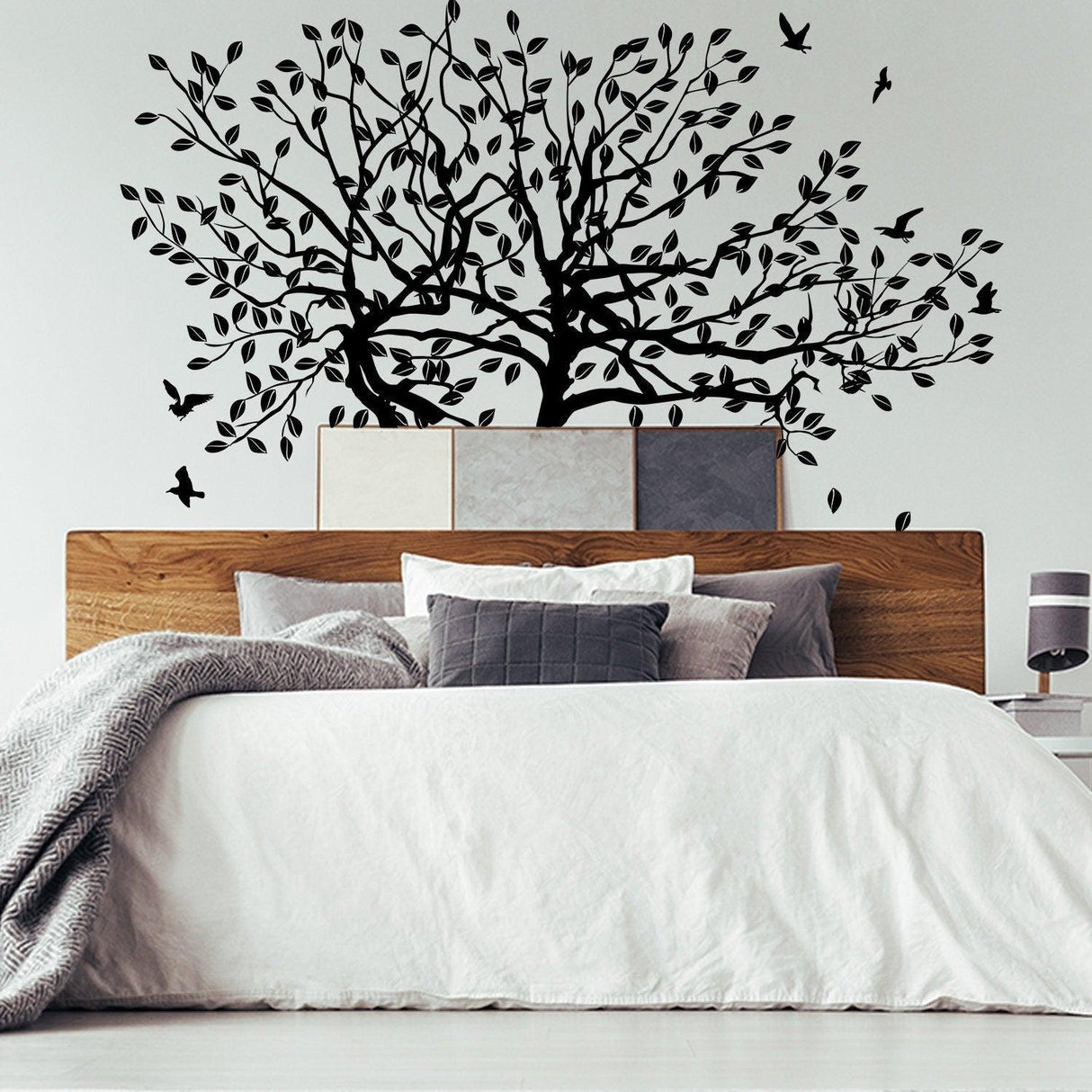 Tree wall decal design with leaves and birds on a bedroom wall above a cozy bed.