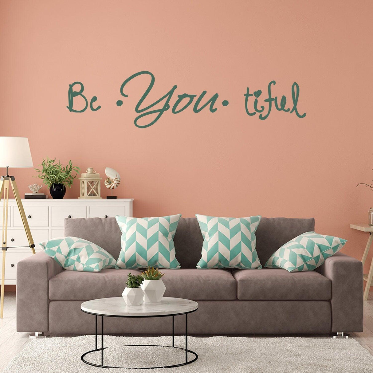 Living room with a 'Be You tiful' wall sticker above a gray sofa with decorative pillows.