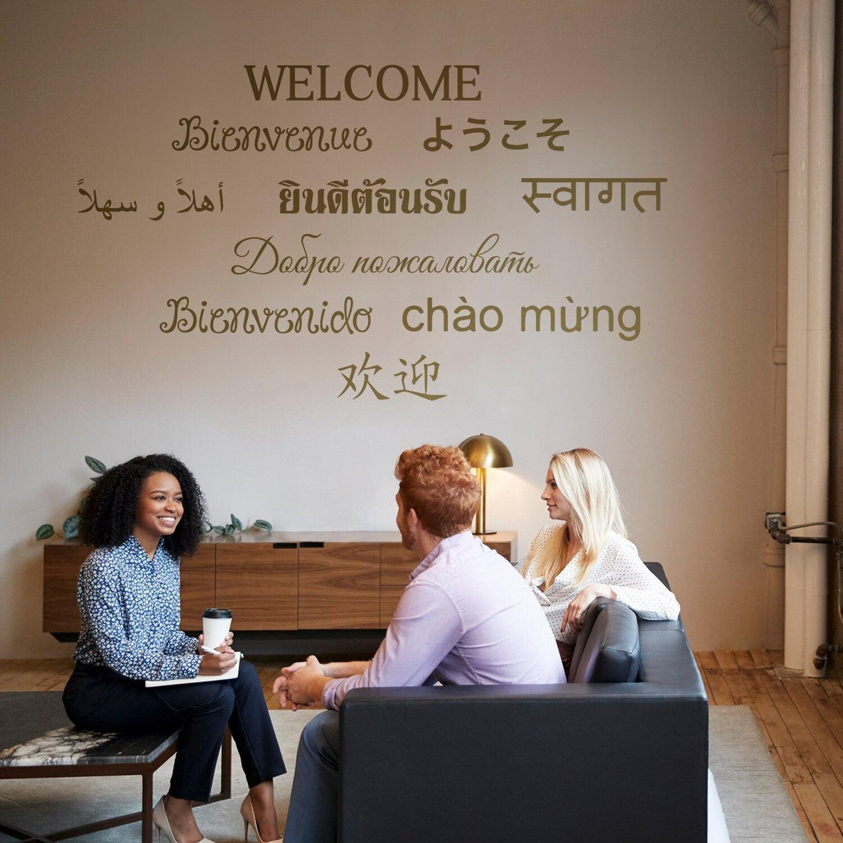 People sitting together in a cozy setting, with a 'Welcome' wall decal in multiple languages behind them.