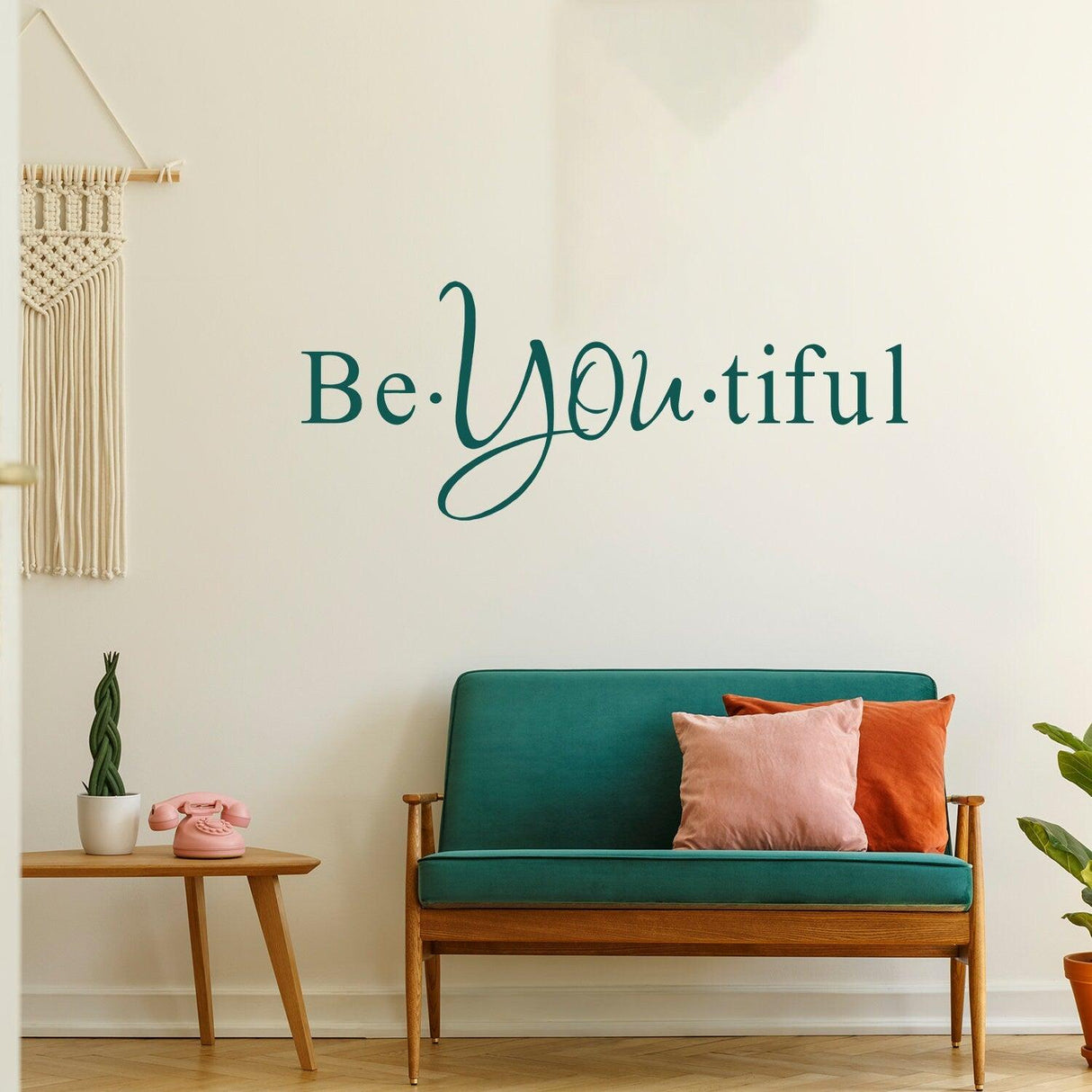 Beautiful vinyl wall sticker 'Be You tiful' in cursive font above a teal sofa surrounded by decorative elements.