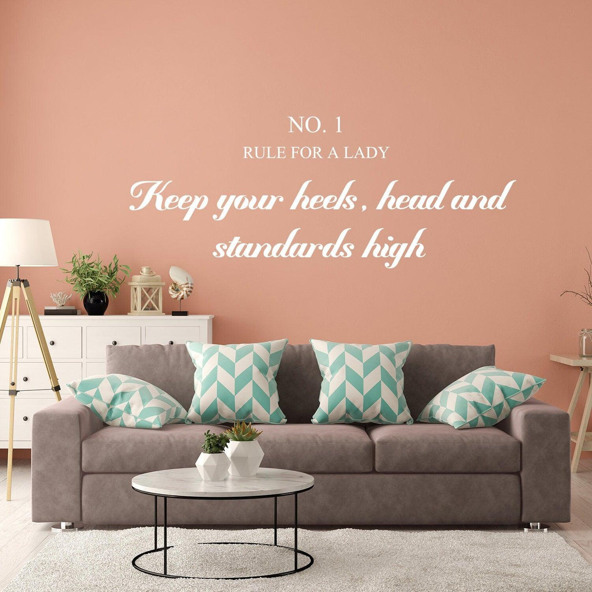 Wall sticker with 'Keep your heels, head, and standards high' quote in stylish font above a gray sofa with teal pillows.