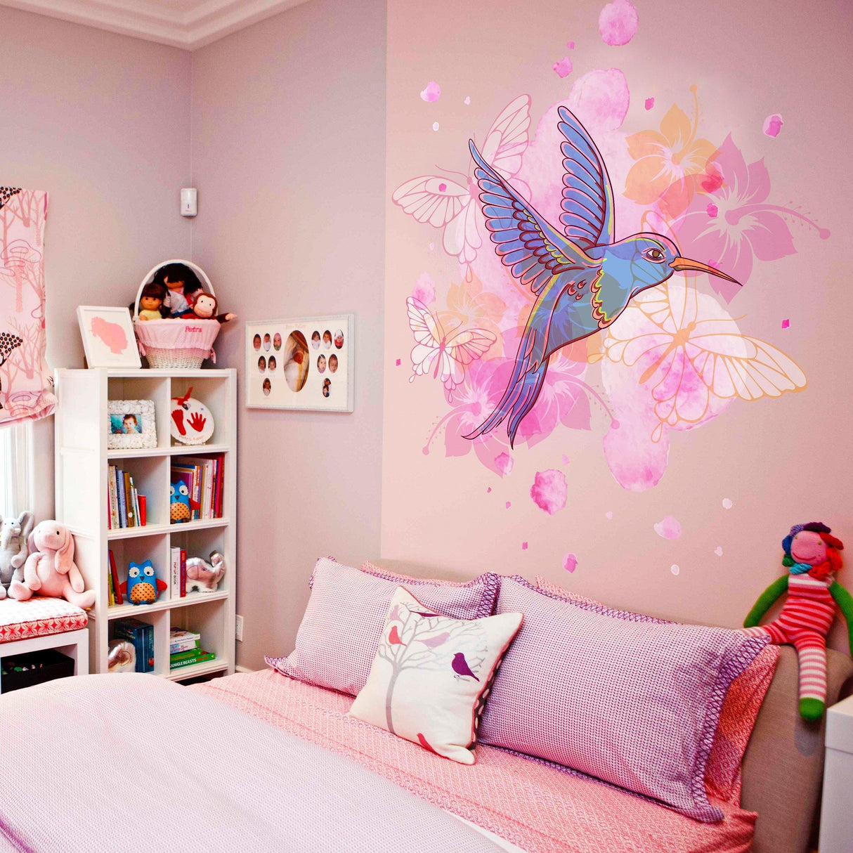Colorful hummingbird vinyl wall sticker on pink bedroom wall with flowers and butterflies, adding vibrant decor.