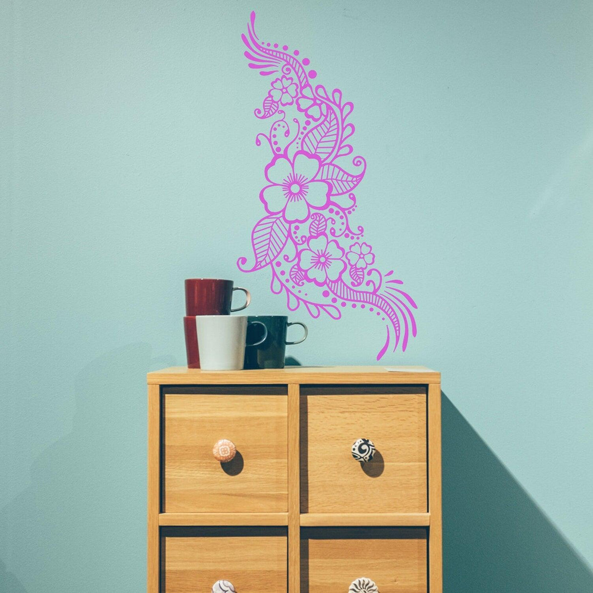 Floral mandala henna tattoo wall vinyl sticker in pink, decorating a beige wall above a wooden cabinet with colorful mugs.