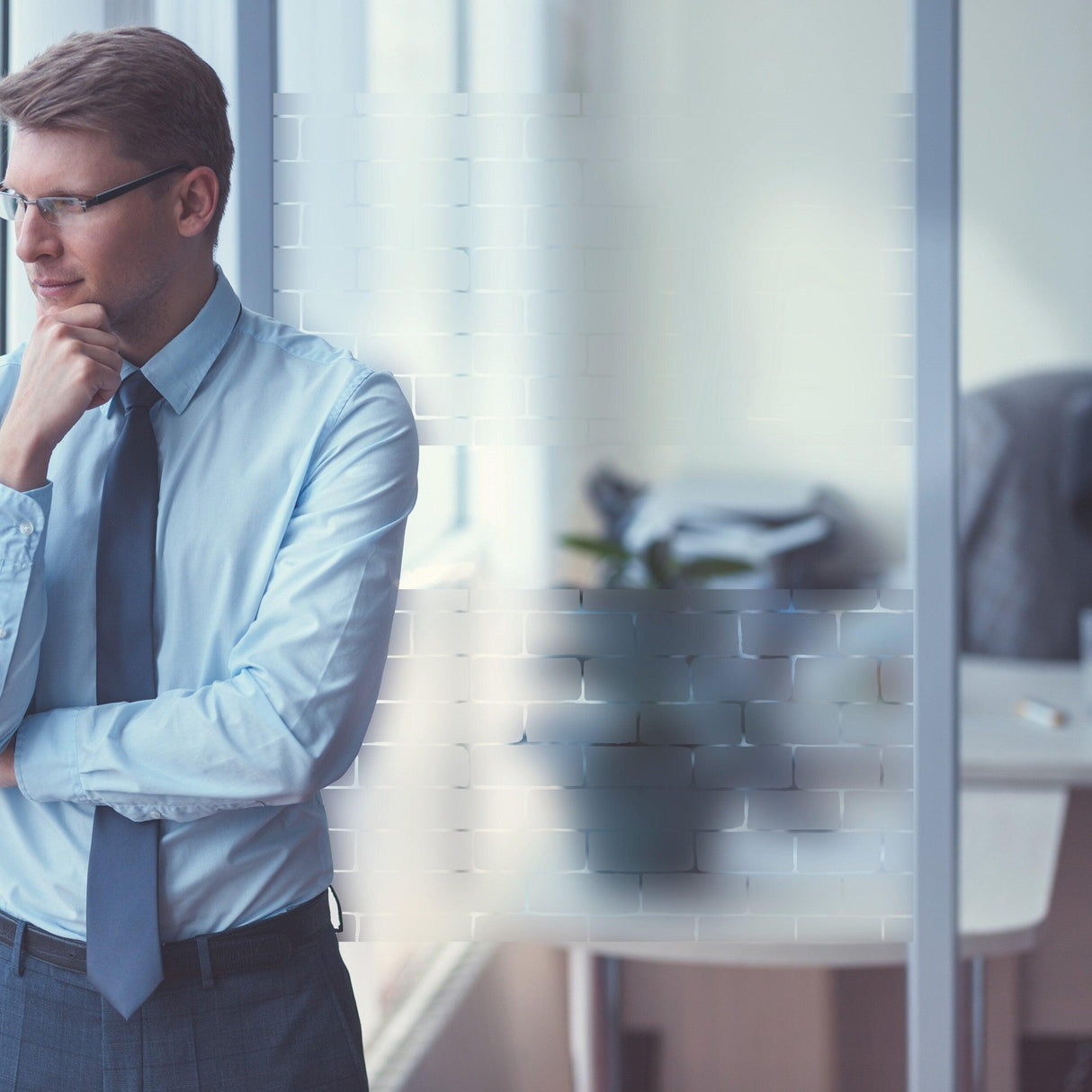 Businessman contemplating near frosted window vinyl decal, enhancing elegance in an office space.