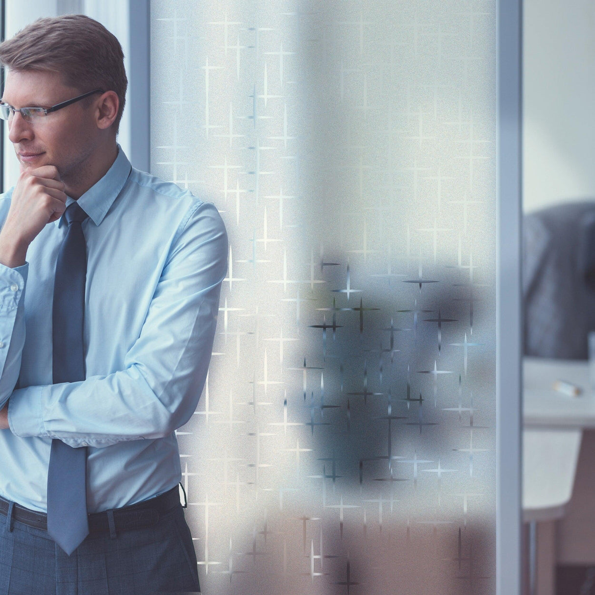 Businessman in a blue shirt and tie standing beside a frosted film window decal, enhancing office aesthetics.