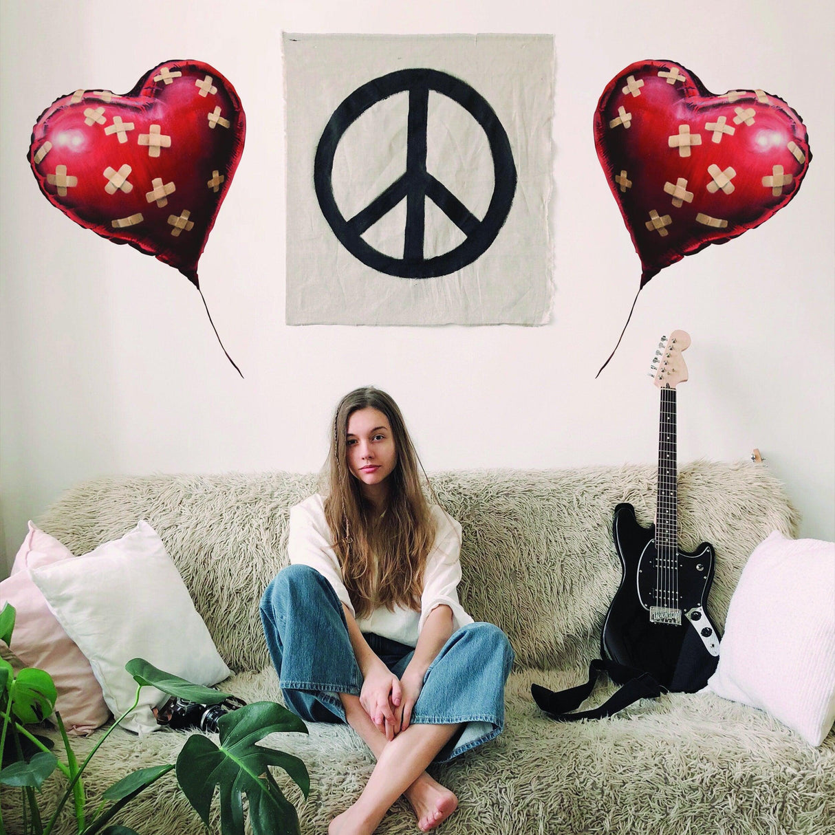 Woman sitting on a couch surrounded by Banksy heart balloon decals and a peace symbol wall art, with guitar nearby.