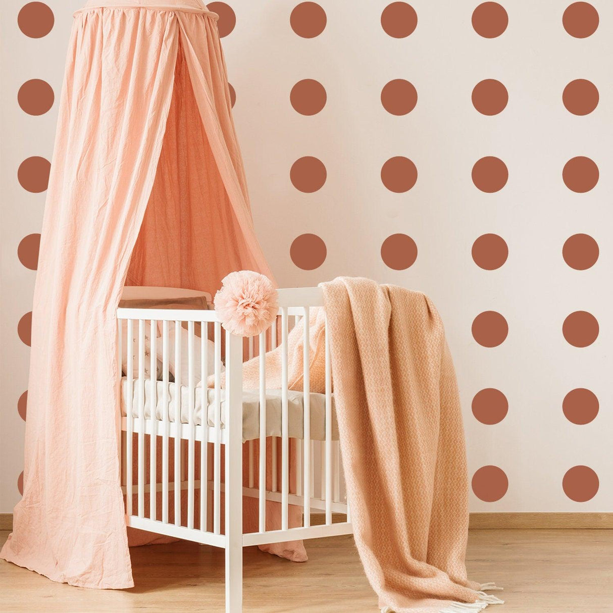 Stylish nursery decor featuring peach-colored canopy, crib, and playful circle wall decals in warm colors.