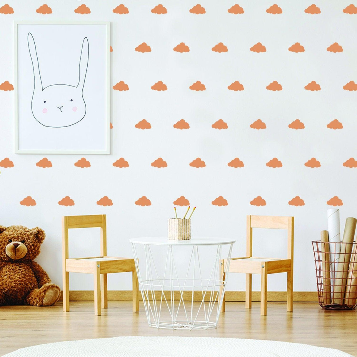 Nursery room with orange cloud wall decals, a bunny art print, and wooden chairs, creating a whimsical baby space.