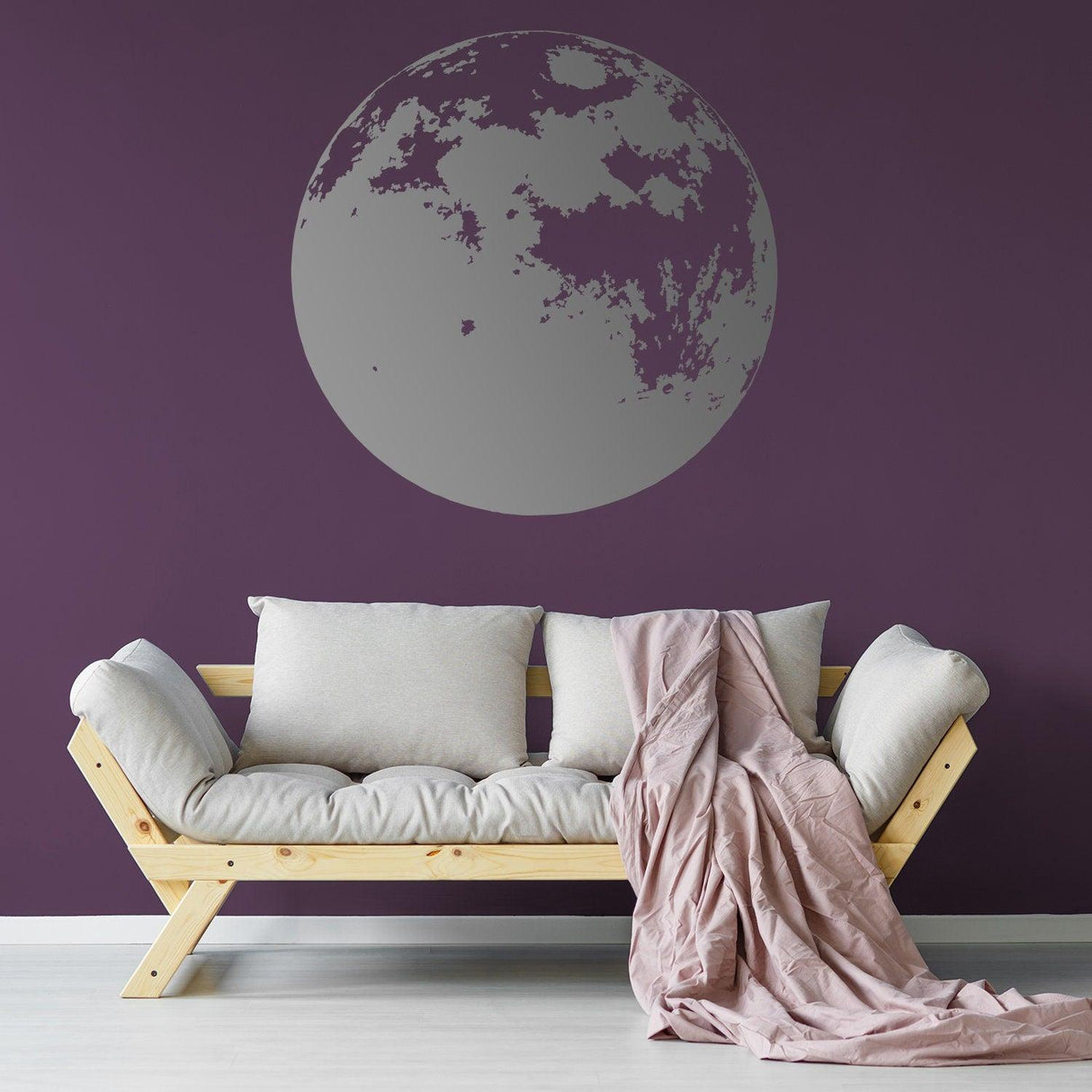 Large silver moon wall decal against a purple wall above a cozy sofa with cushions and a soft blanket.