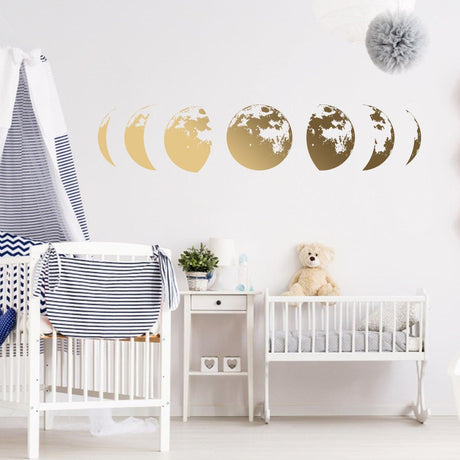 Gold moon phases wall decor decal in nursery with crib and teddy bear, adding elegance and charm to the space.
