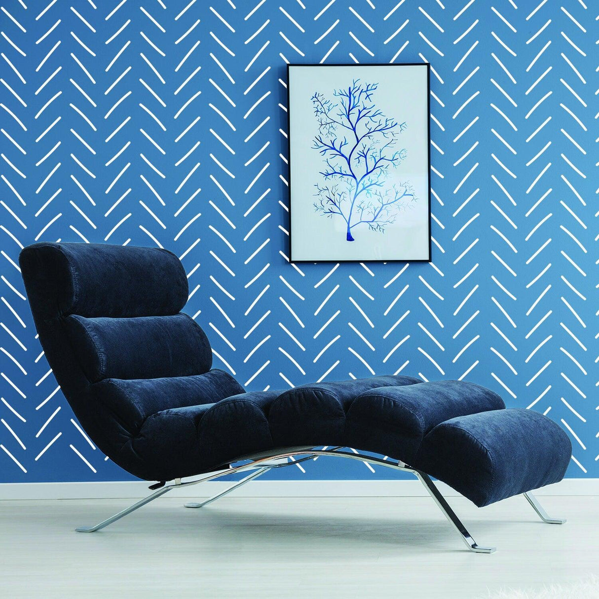 Modern blue wall with herringbone wallpaper pattern, stylish lounge chair, and framed tree artwork.