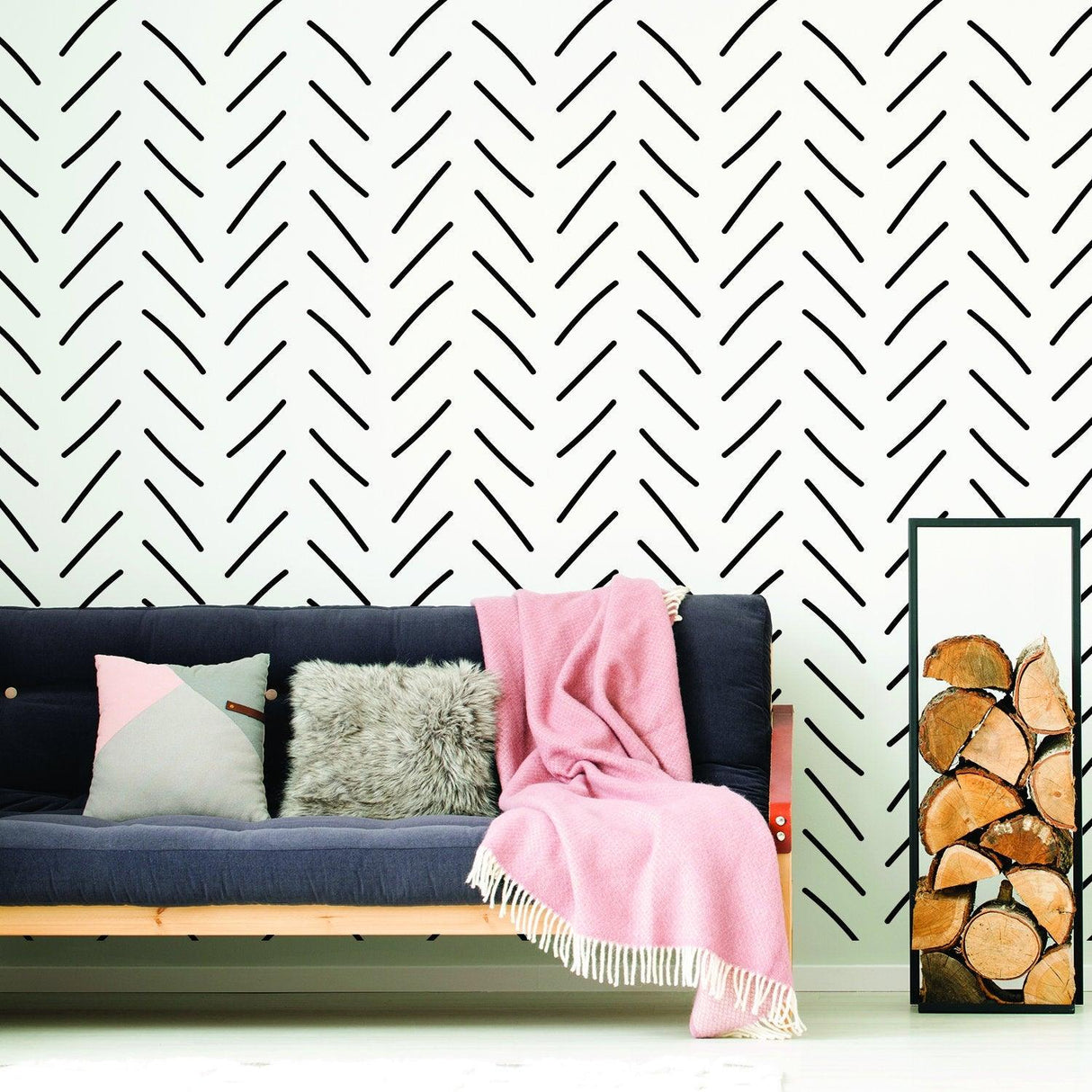 Stylish herringbone wallpaper in black on a white wall behind a cozy seating area with cushions and a pink throw.