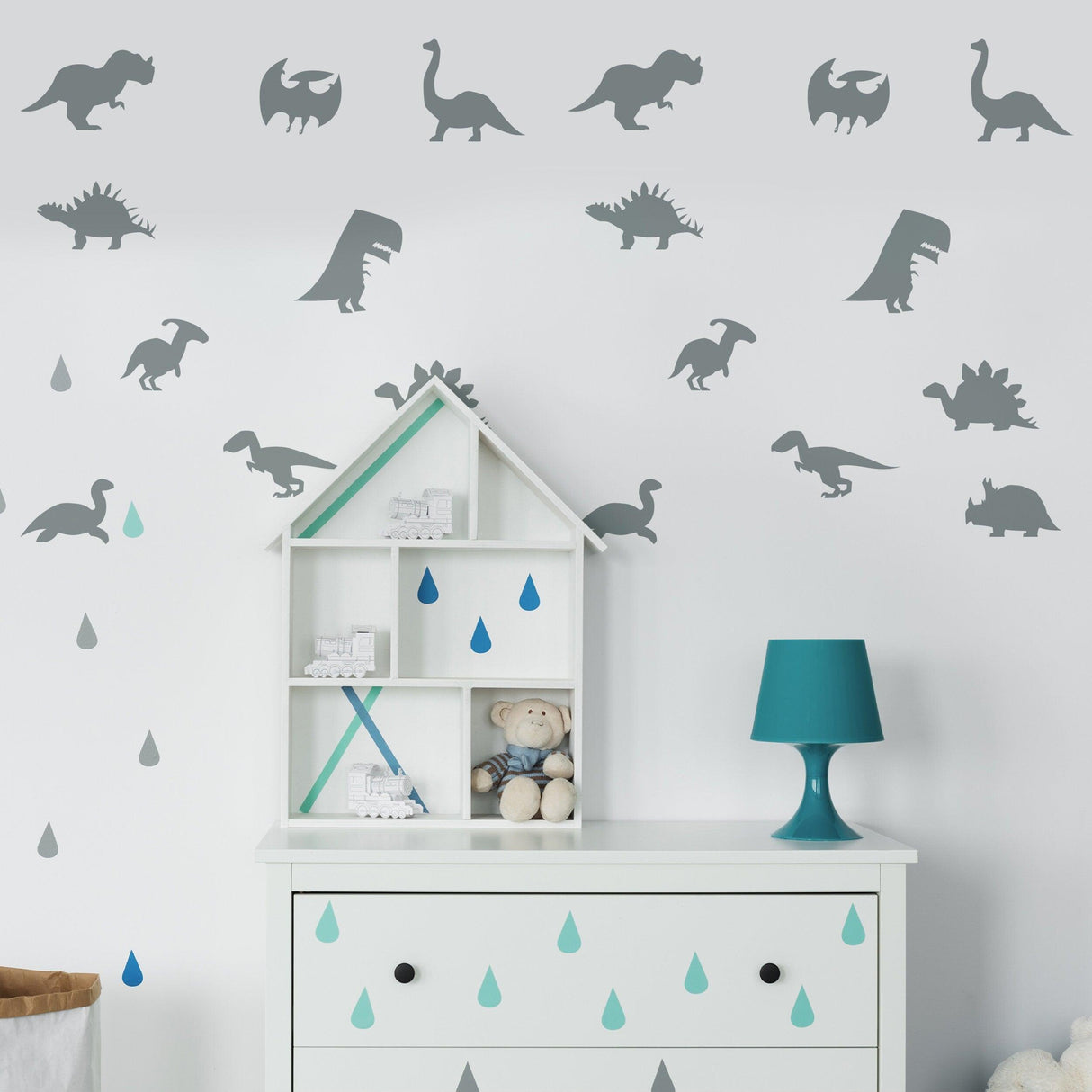Gray dinosaur silhouette wall decals in a nursery, featuring various dino designs above a white shelf and teal lamp.