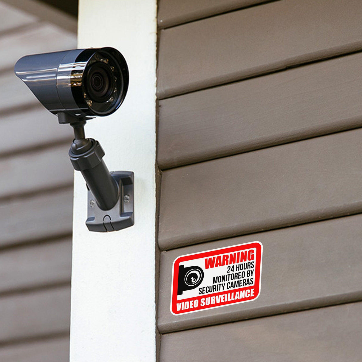 Video surveillance camera with warning sign indicating 24-hour security monitoring on a wooden wall.
