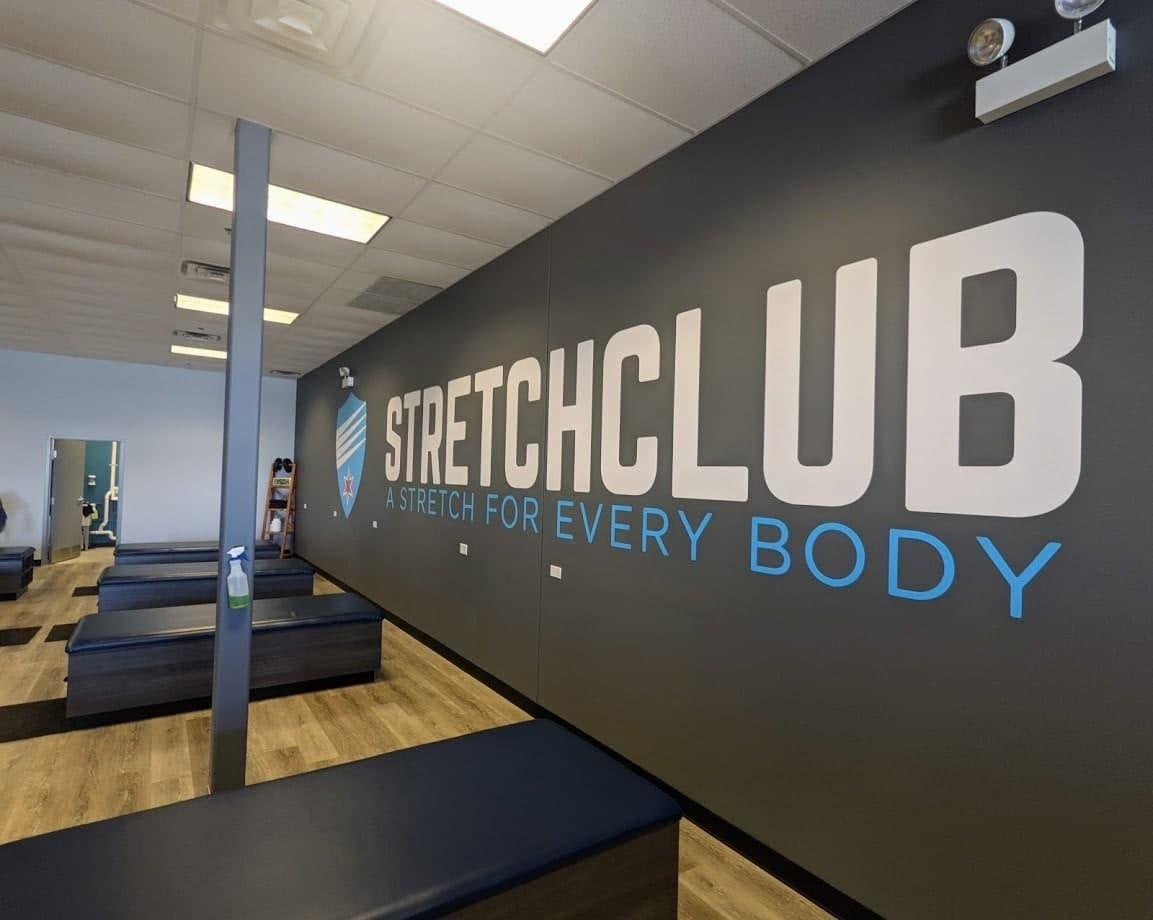 Interior view of Stretch Club featuring logo and slogan on wall, with seating areas for stretching.