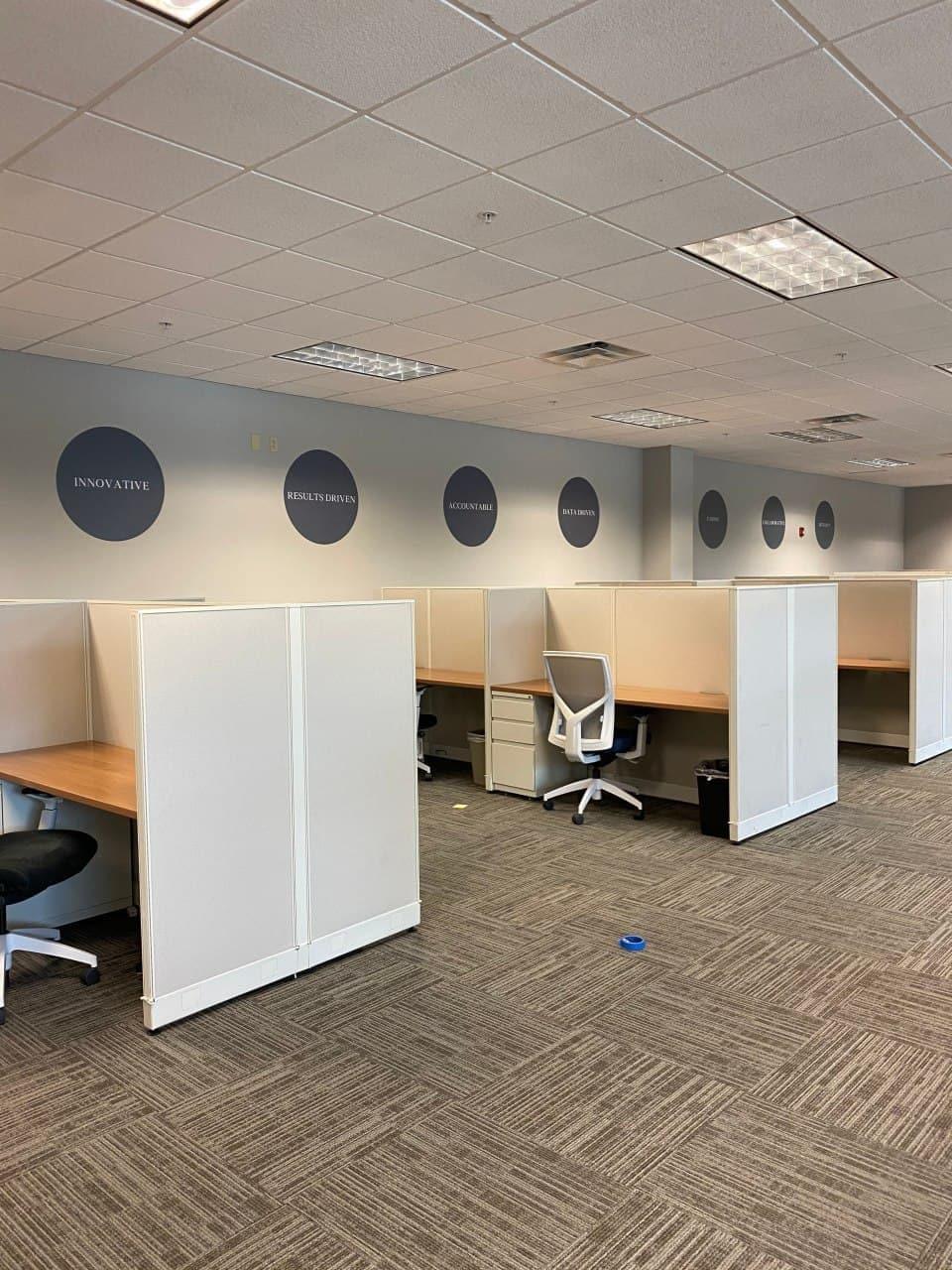 Modern office space with cubicles and motivational wall decals like 'Innovative' and 'Results Driven'.