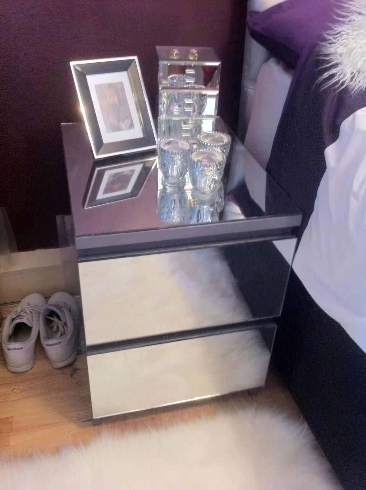 Mirrored nightstand with a photo frame and decorative items, placed beside a bed with white fur rug.