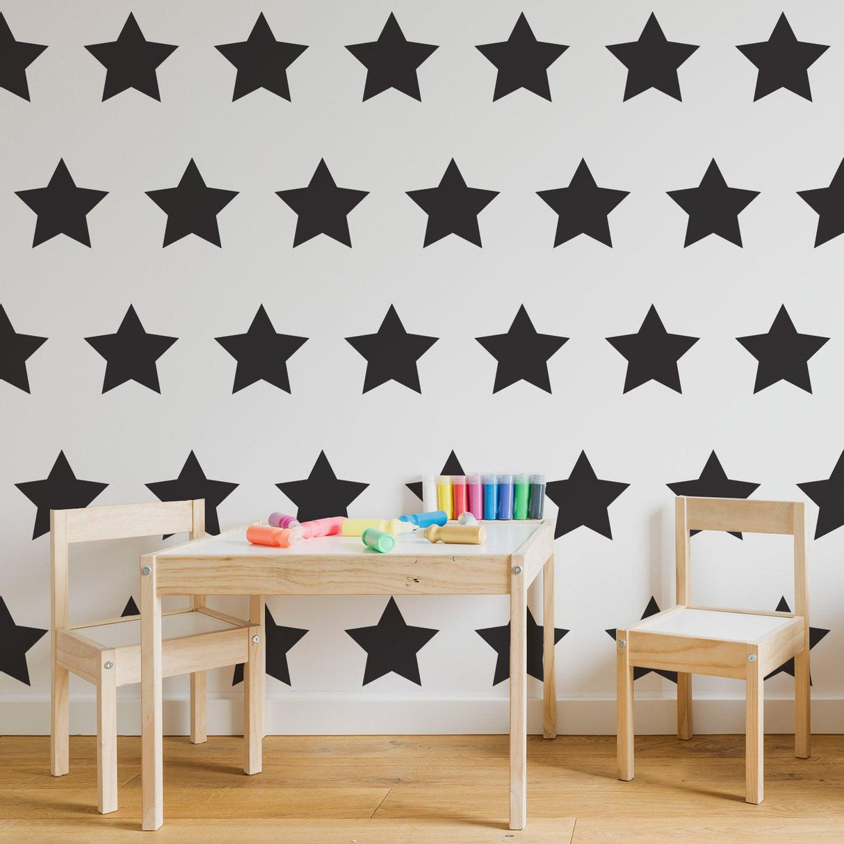 Nursery with black star wall decals, featuring a wooden table and chairs with colorful craft supplies.