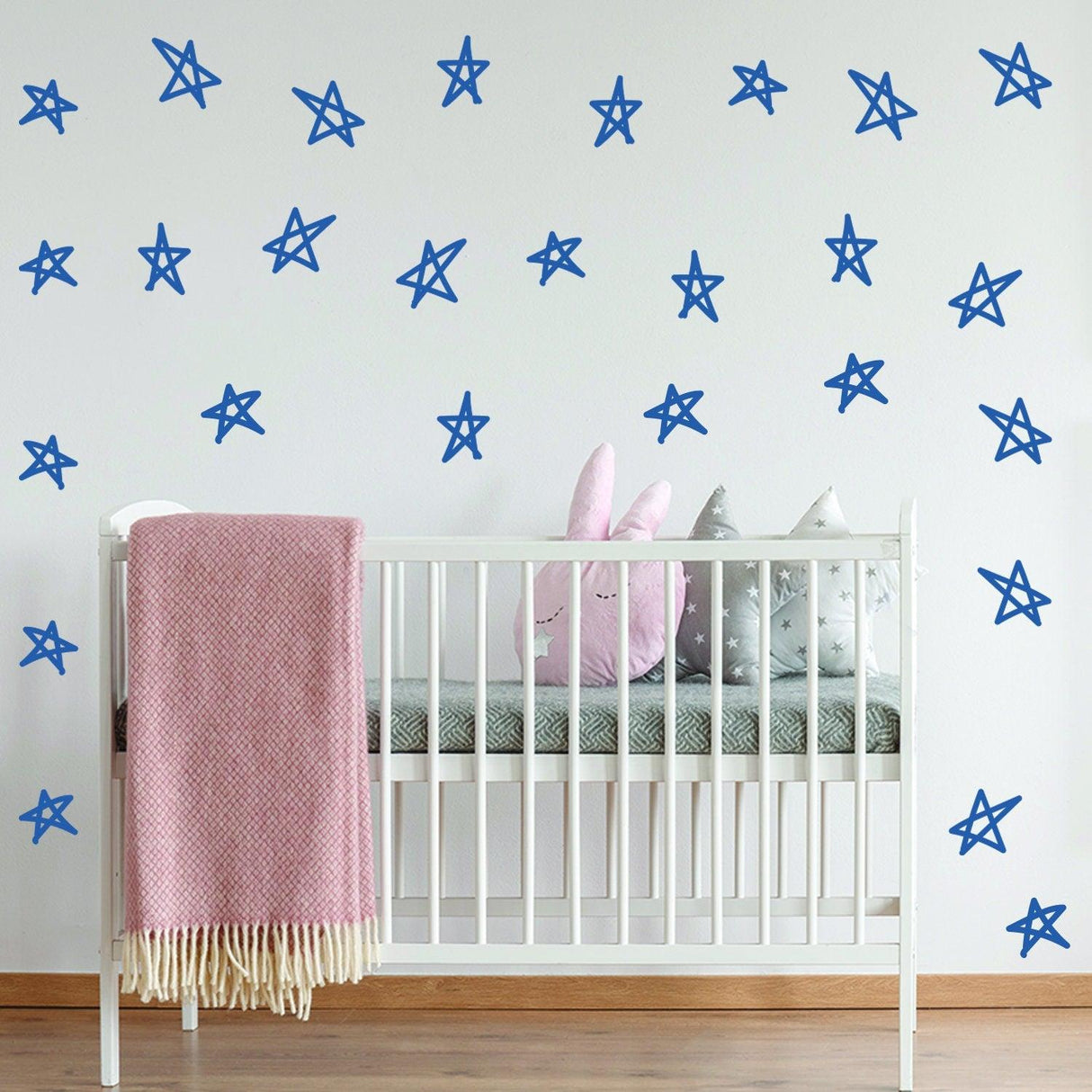 Nursery wall with blue star decals and a crib featuring a pink blanket and plush toys.