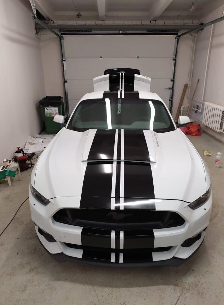 Custom white car with black racing stripes parked in a garage, showcasing sporty design and modifications.