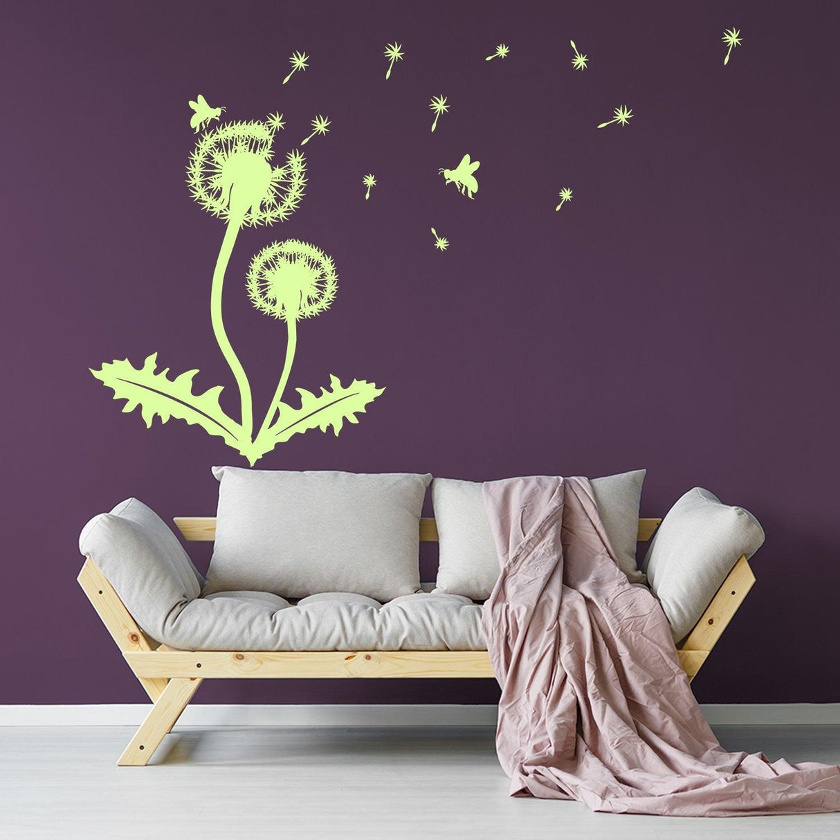 Large dandelion wall decor decal glowing on a dark wall above a cozy sofa with blankets.