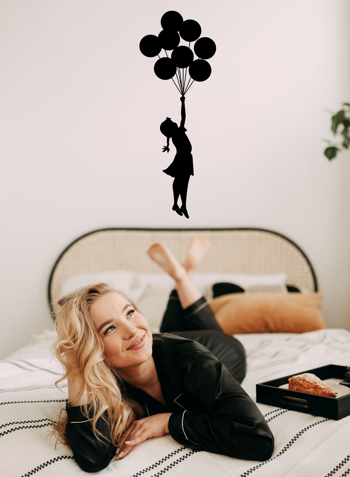 Banksy Girl With Balloons Wall Decal above a woman relaxing on a bed, adding artistic flair to the room.