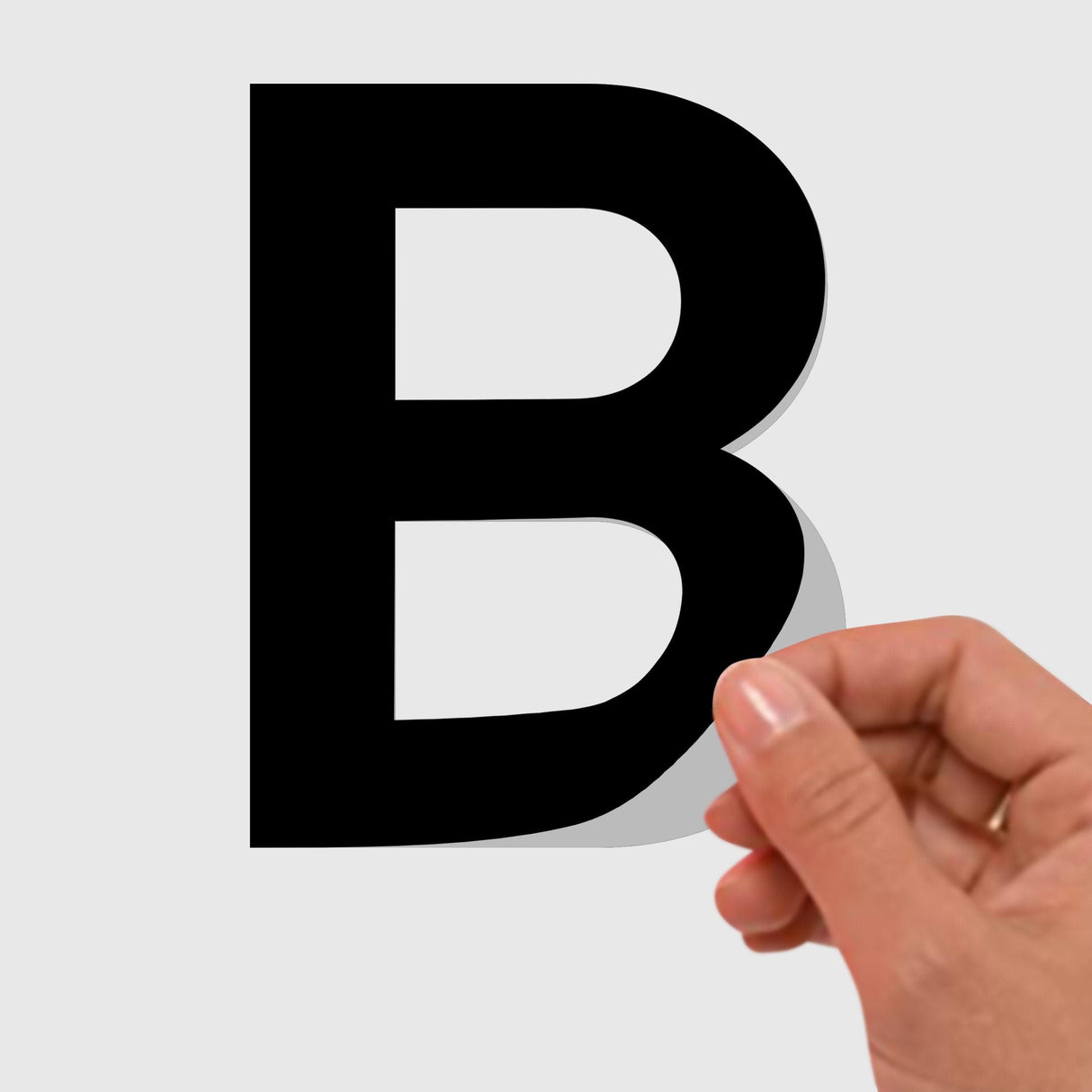 Hand applying a black vinyl removable letter sticker of the letter B on a light background.