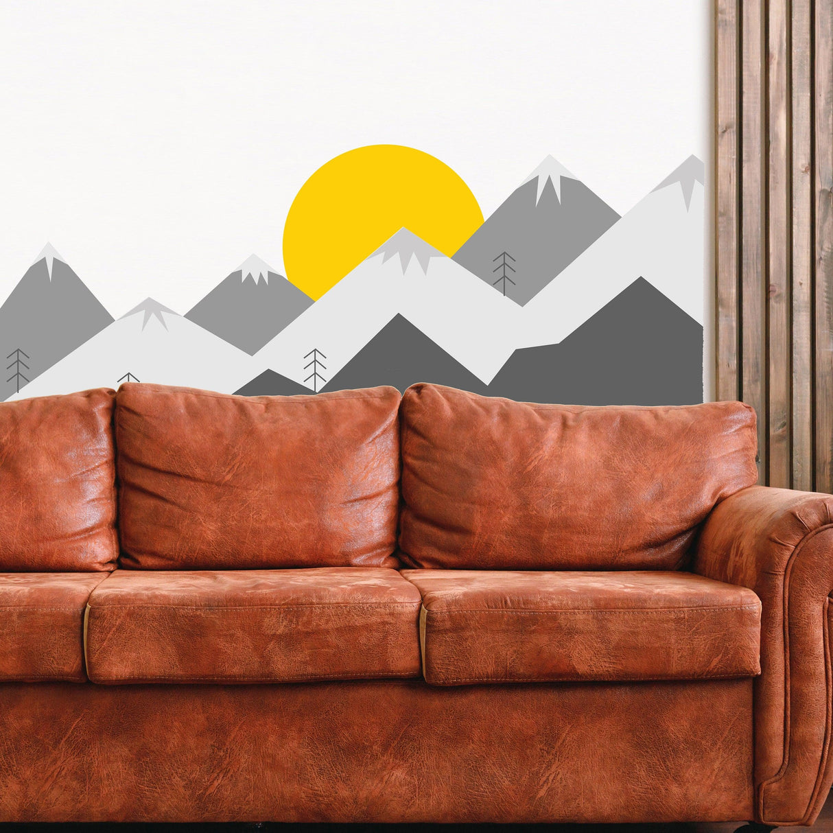 Mountain wall decal featuring grey peaks and vibrant sun above a brown leather couch in a nursery.